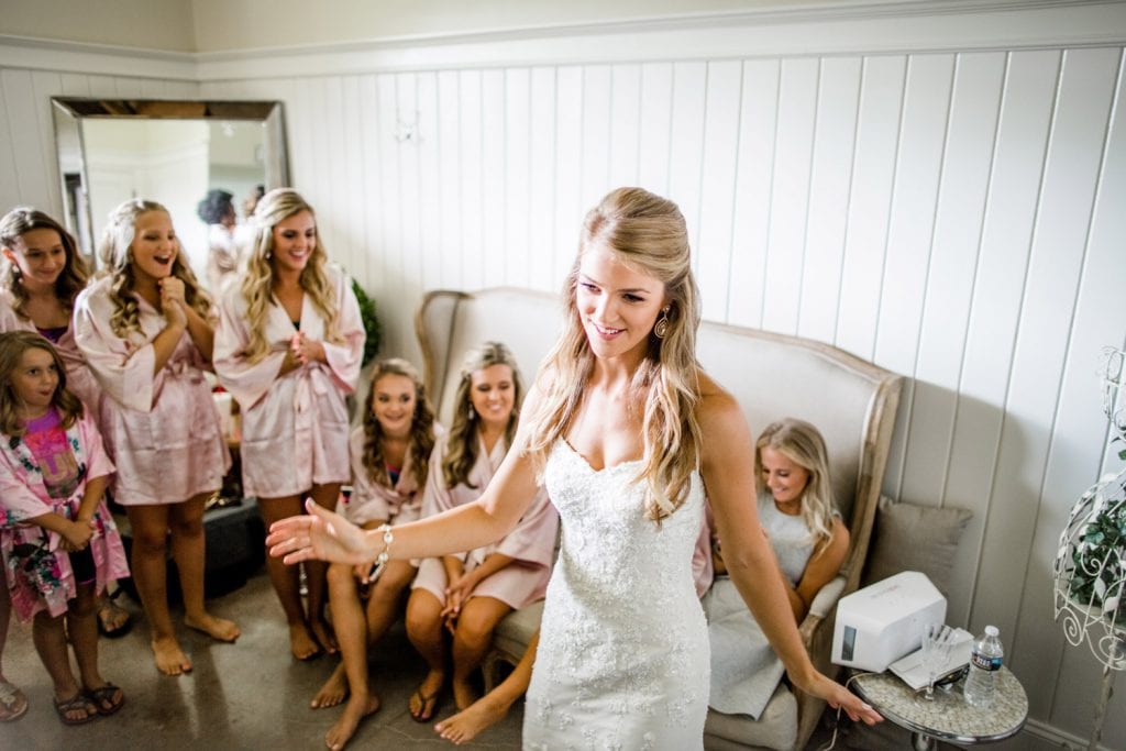 Bride showing off dress in bridal room with bridesmaids