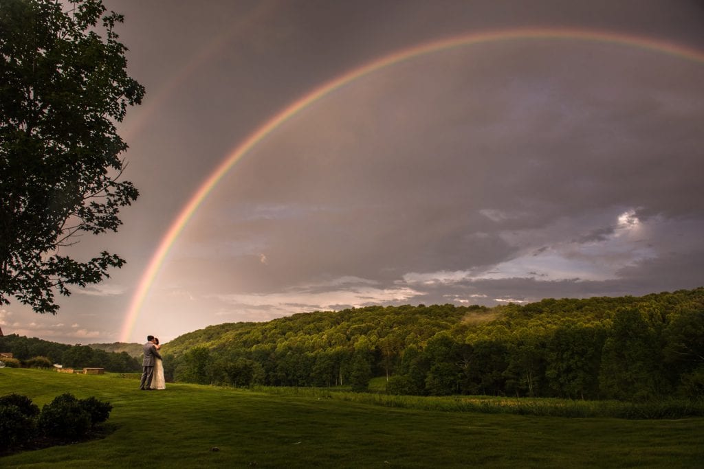 Bride and groom hold each other in front of rainbow