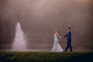 Bride leads groom by the fountain